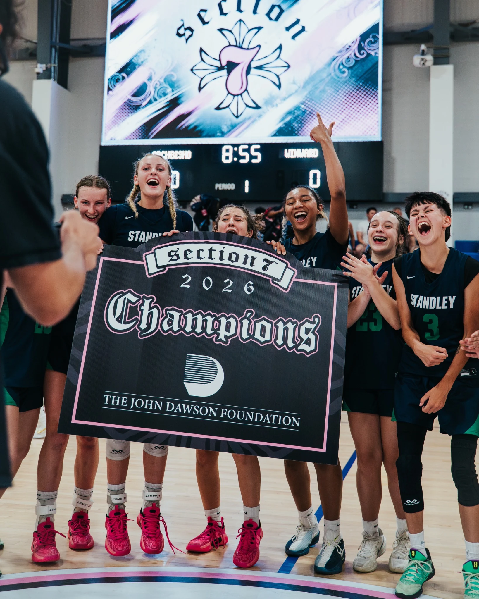 Girls basketball players celebrating with a Section 7 championship sign