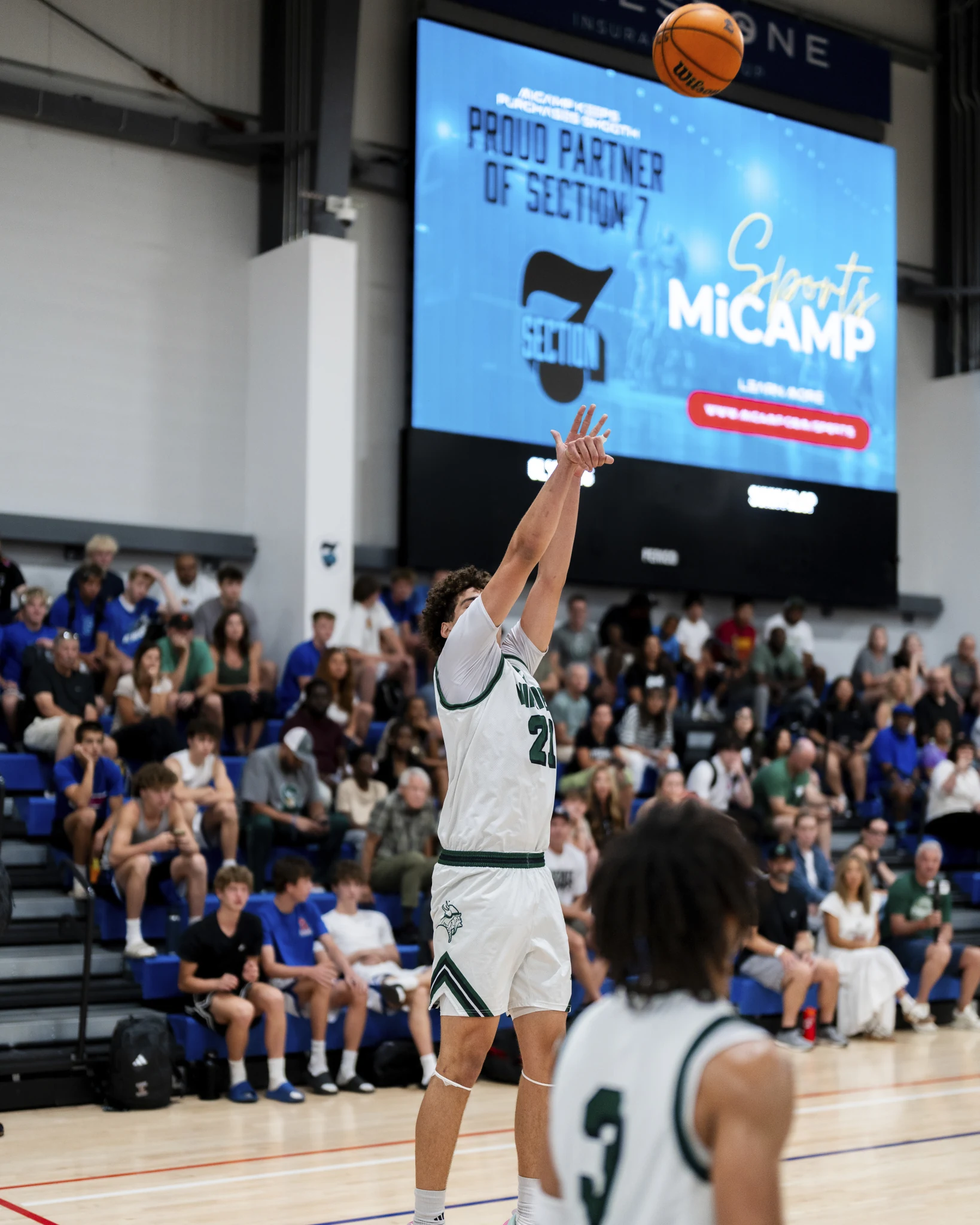 A high school basketball player shooting with a full courtside crowd behind him